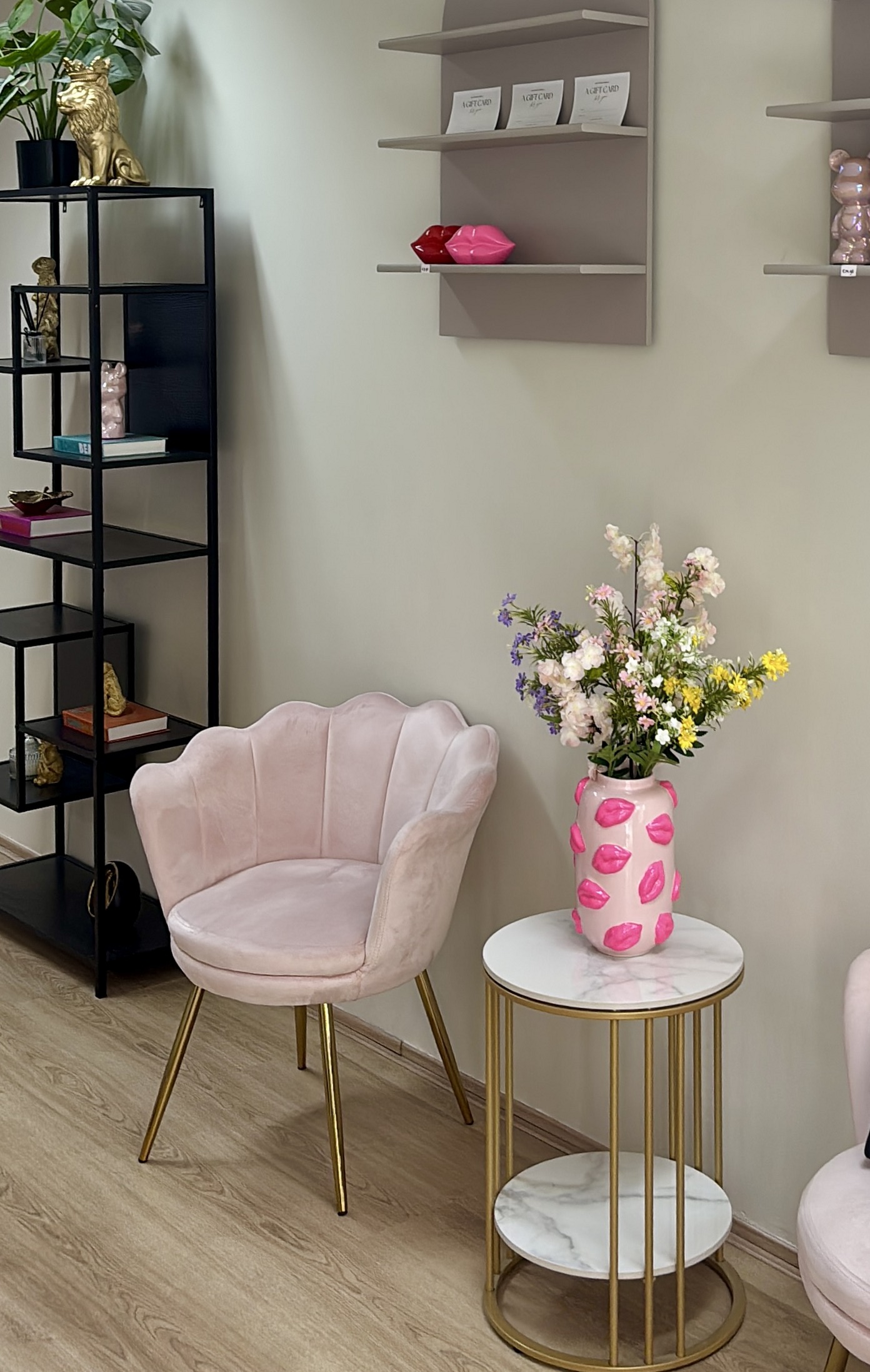 Hoekje in de salon met een roze schelpstoel, bloemen en een bijzettafel met gouden rand